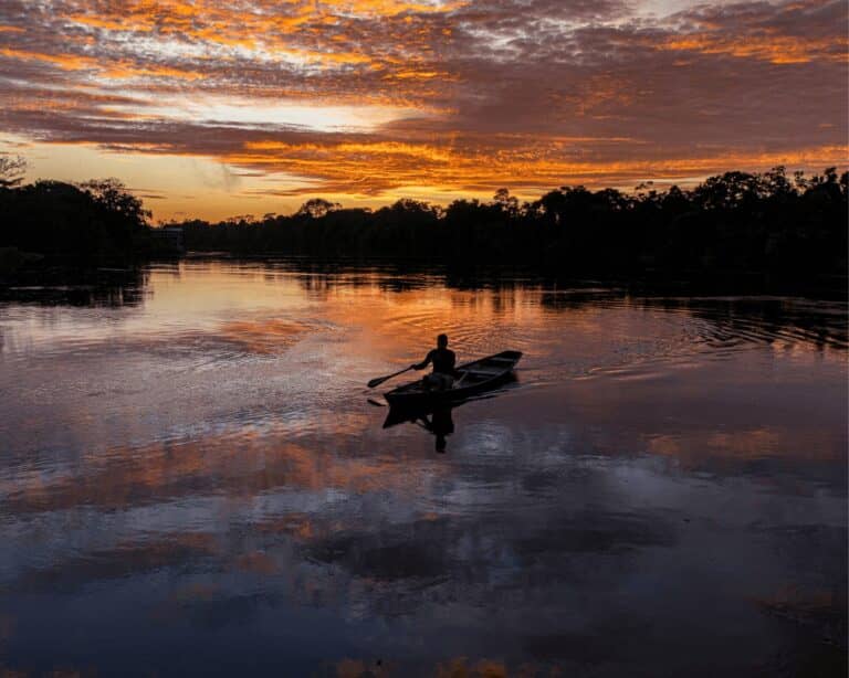 Person paddling a wooden canoe on a calm rainforest river at sunset, a classic moment on an Amazon tour from Manaus
